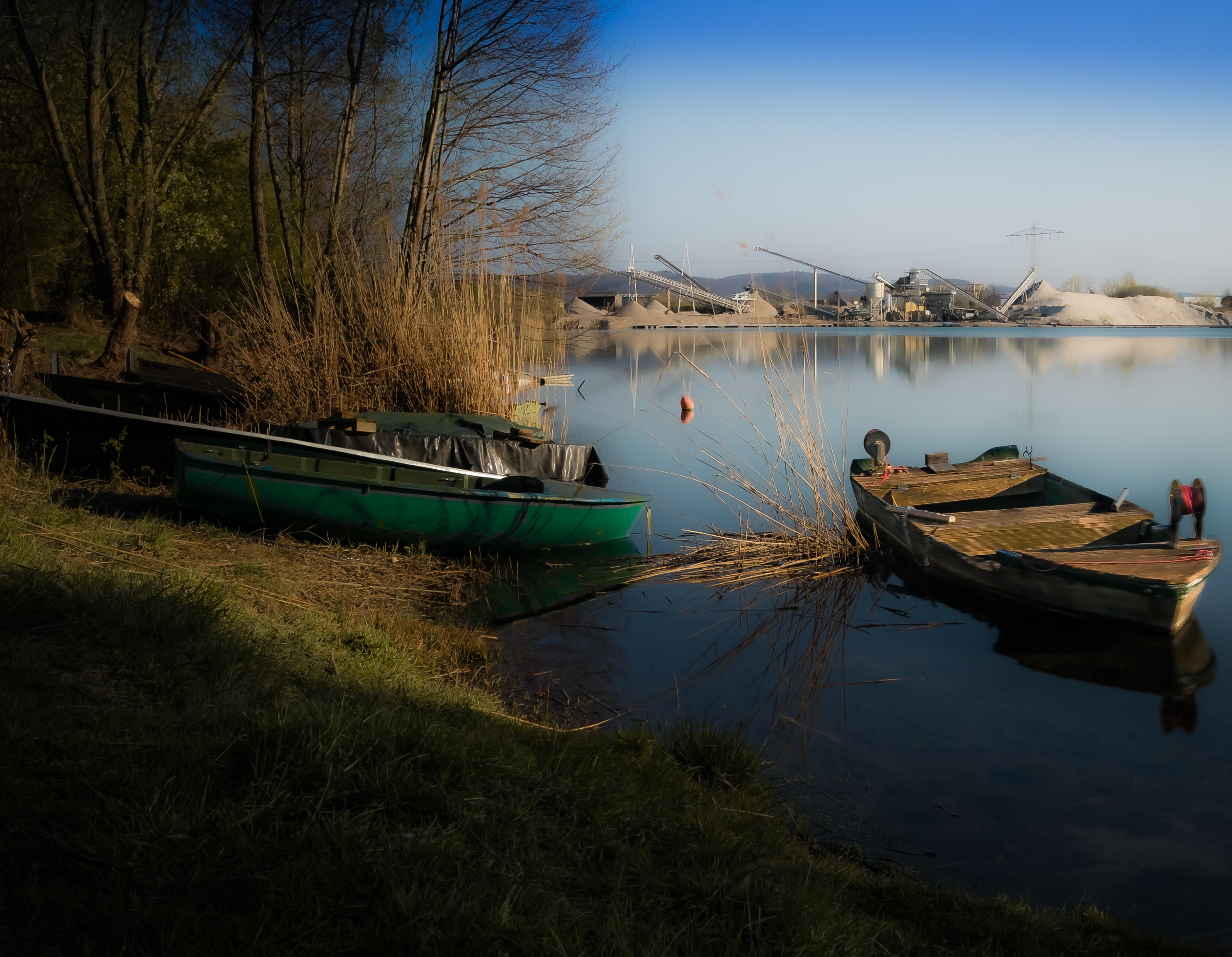 Boote am Ufer eines Sees mit Kieswerk im Hintergrund